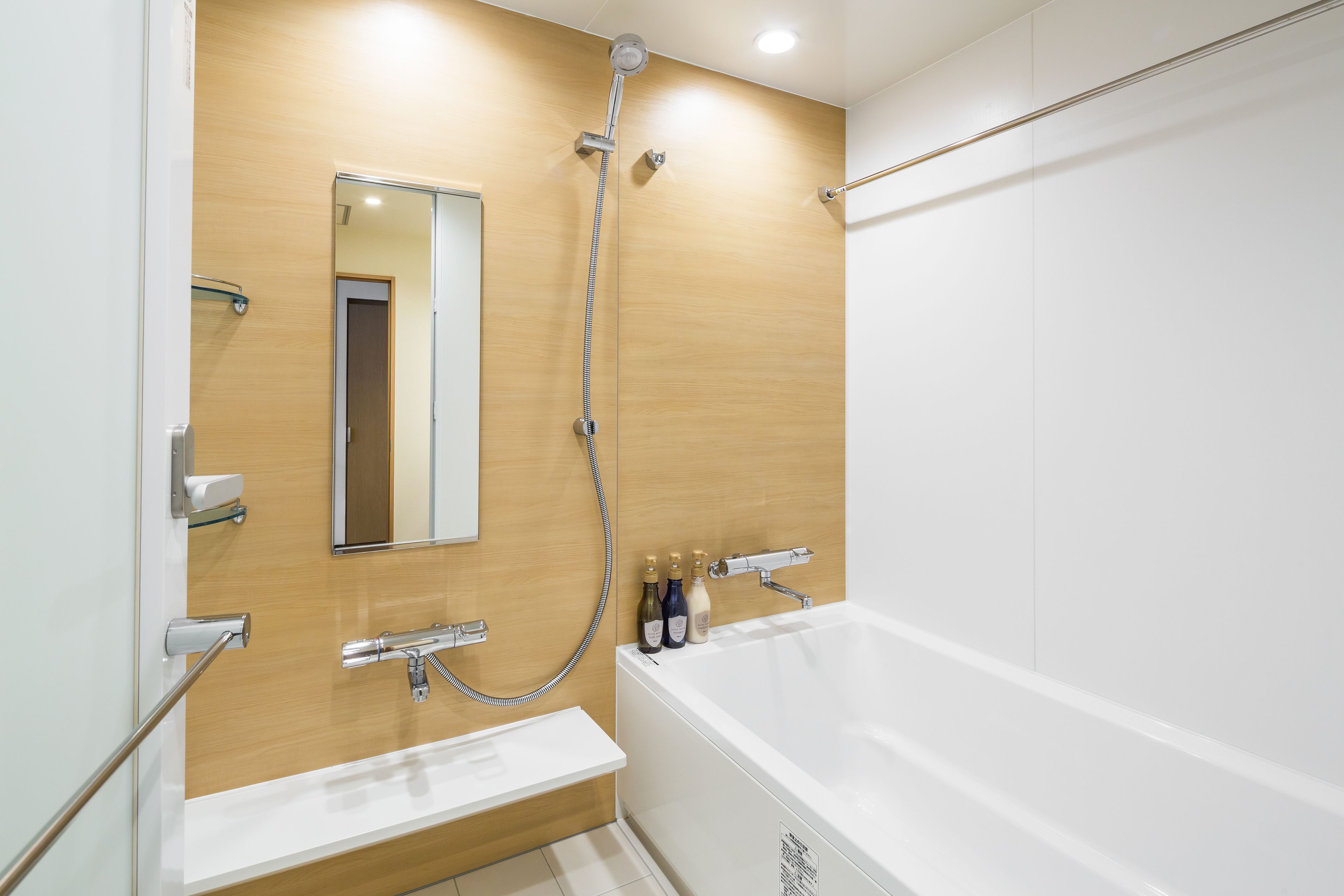 Ein modernes Badezimmer mit Holzwand, einer weißen Badewanne, einer Duschbrause und einem Spiegel.