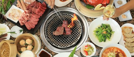 A table with various dishes, including seafood, vegetables, and meat, and a grill with meat being cooked.