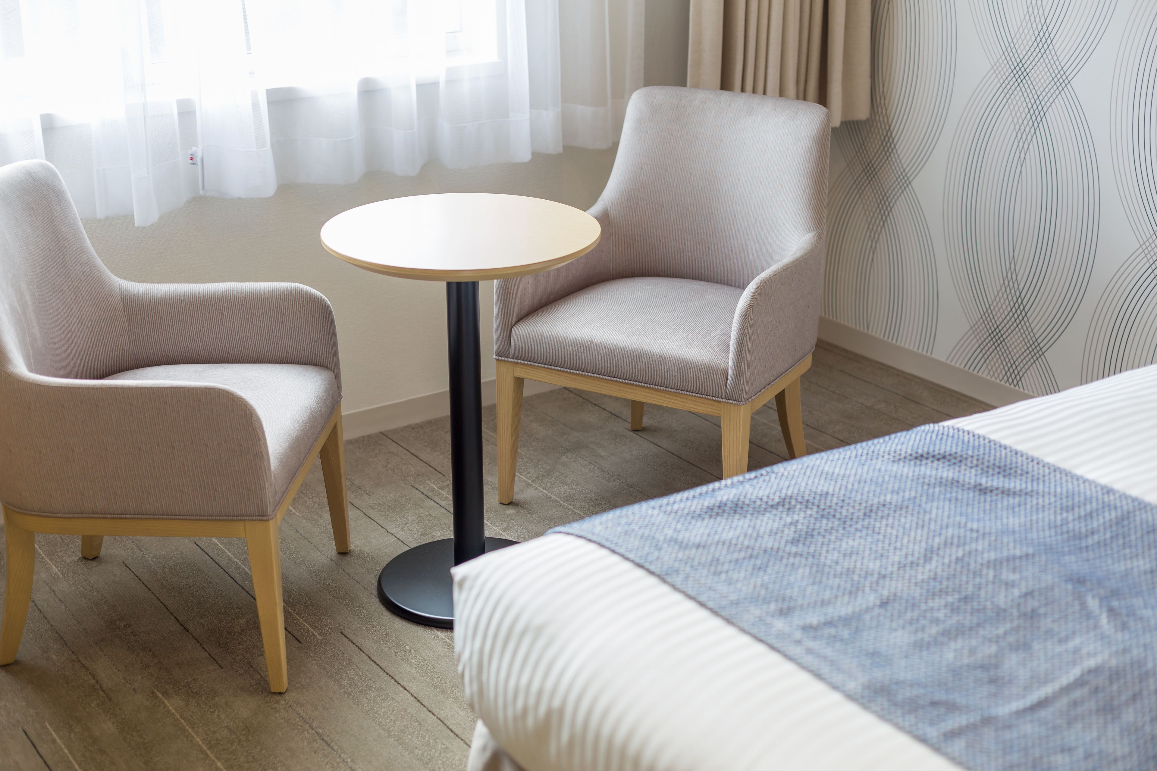 A hotel room with two armchairs, a round table, and a bed with a blue blanket.