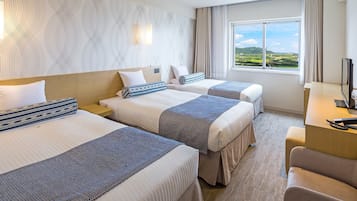 A hotel room with two beds, a desk, and a large window offering a view of the countryside.