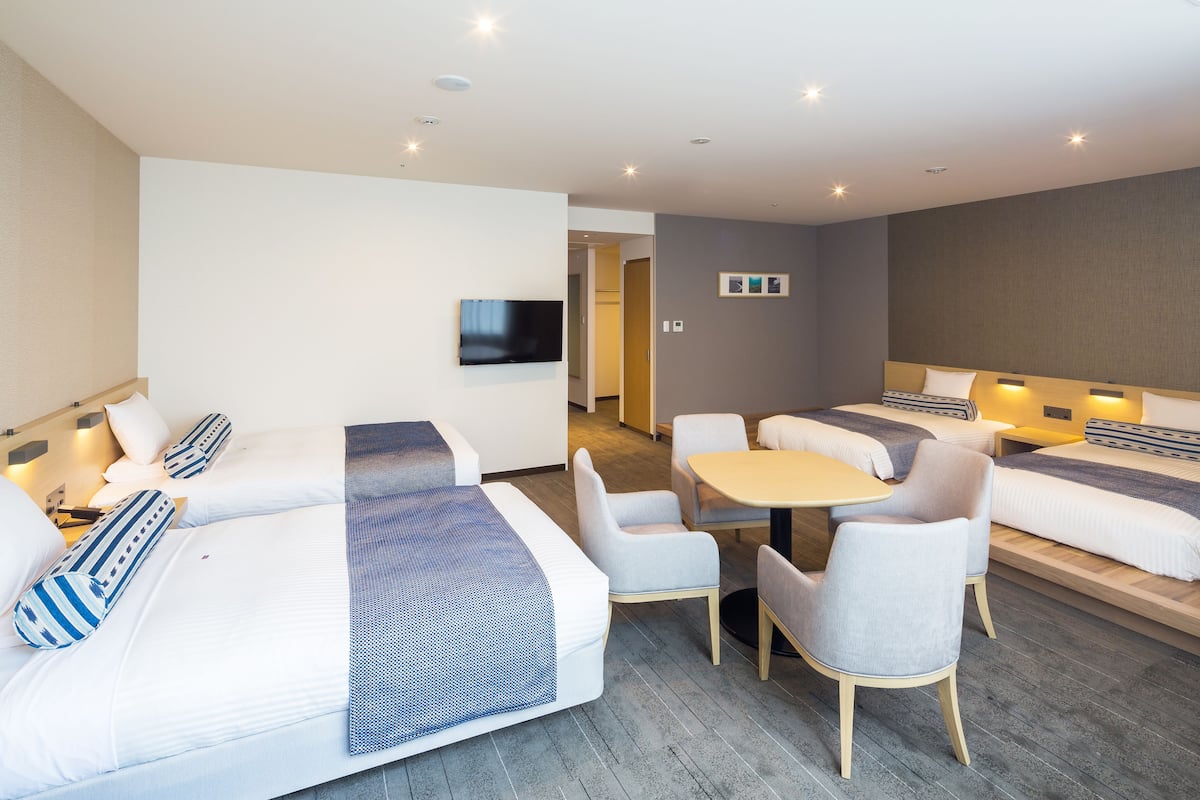 A modern hotel room with two beds, a flat-screen TV, a small dining table, and a seating area.
