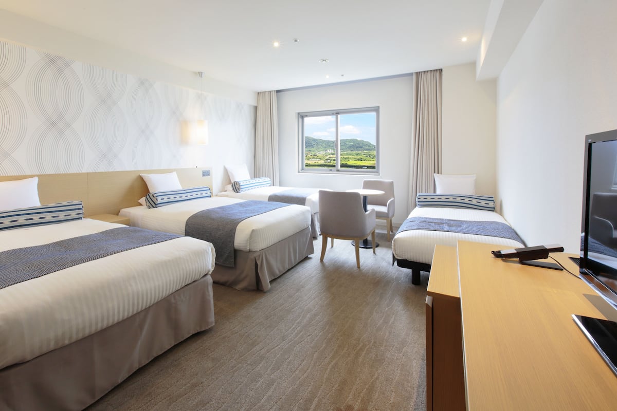 A hotel room with two beds, a desk, a chair, and a TV.