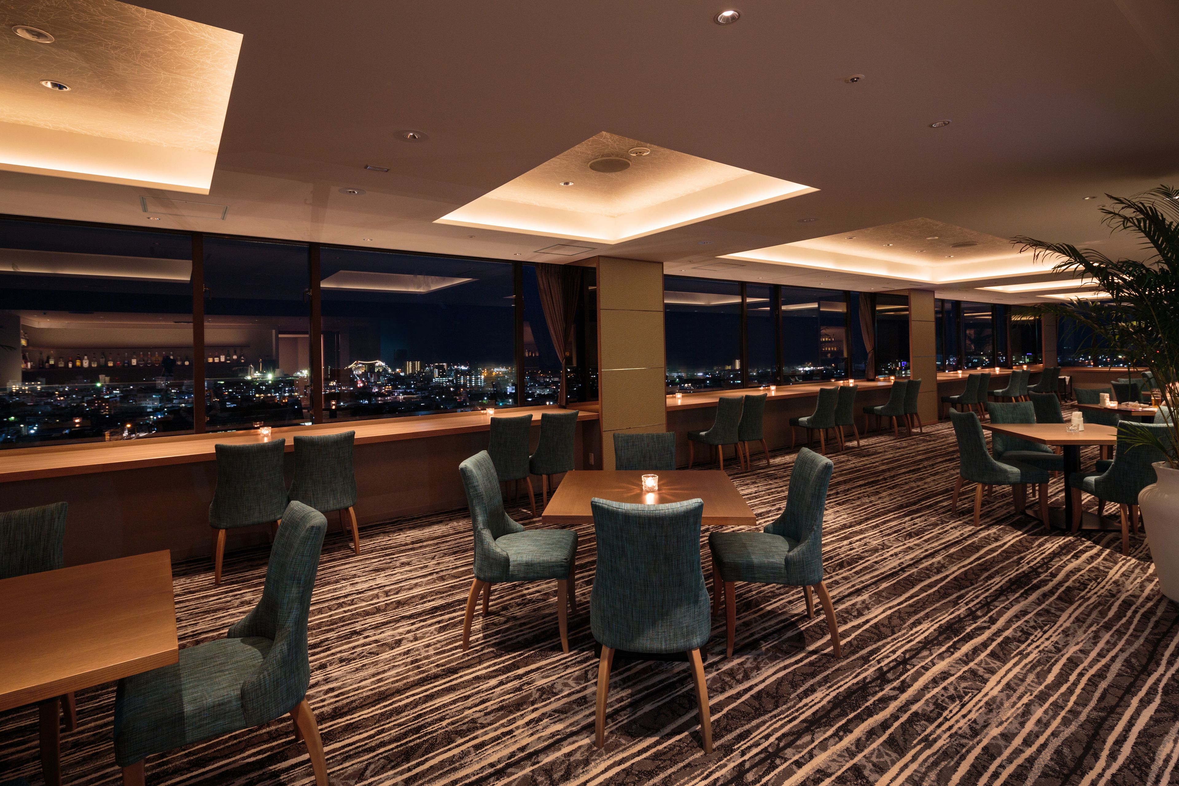 A modern hotel lobby with a panoramic city view, comfortable seating, and a patterned carpet.