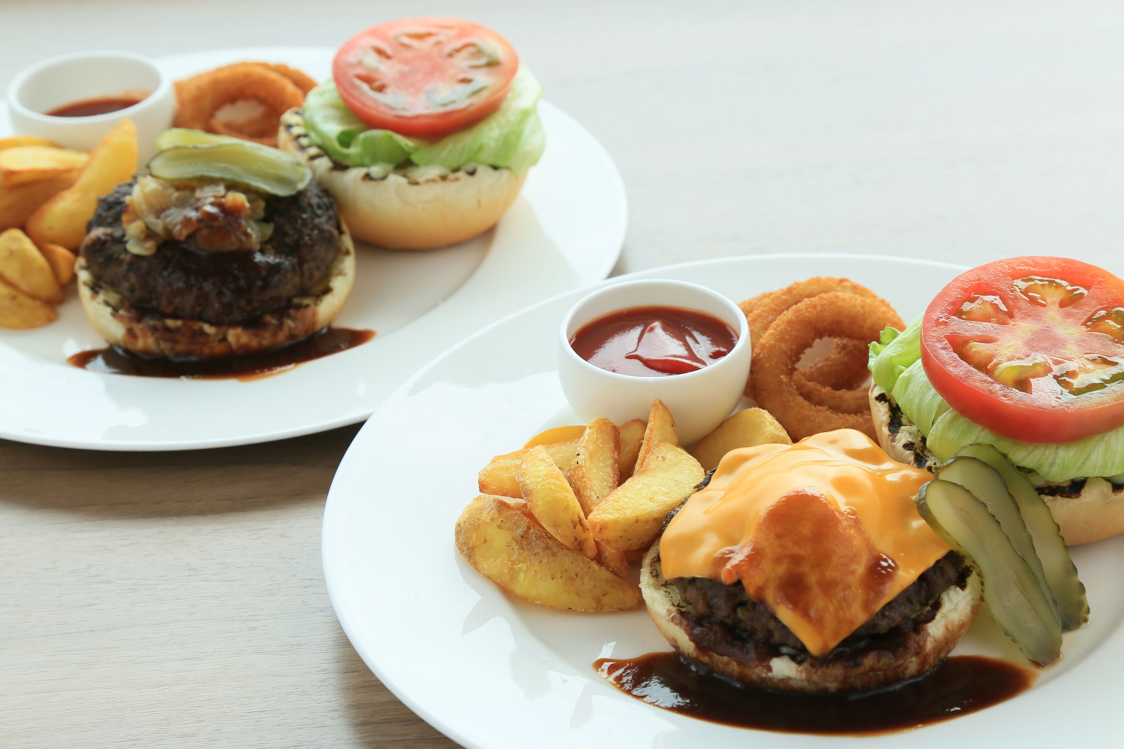Two plates of burgers with fries and ketchup.