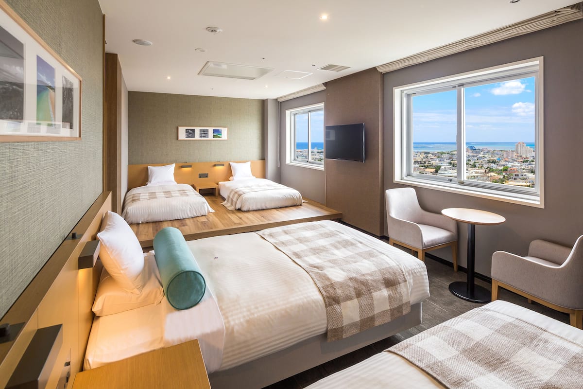 A hotel room with two beds, a TV, a small table, and a view of the city.