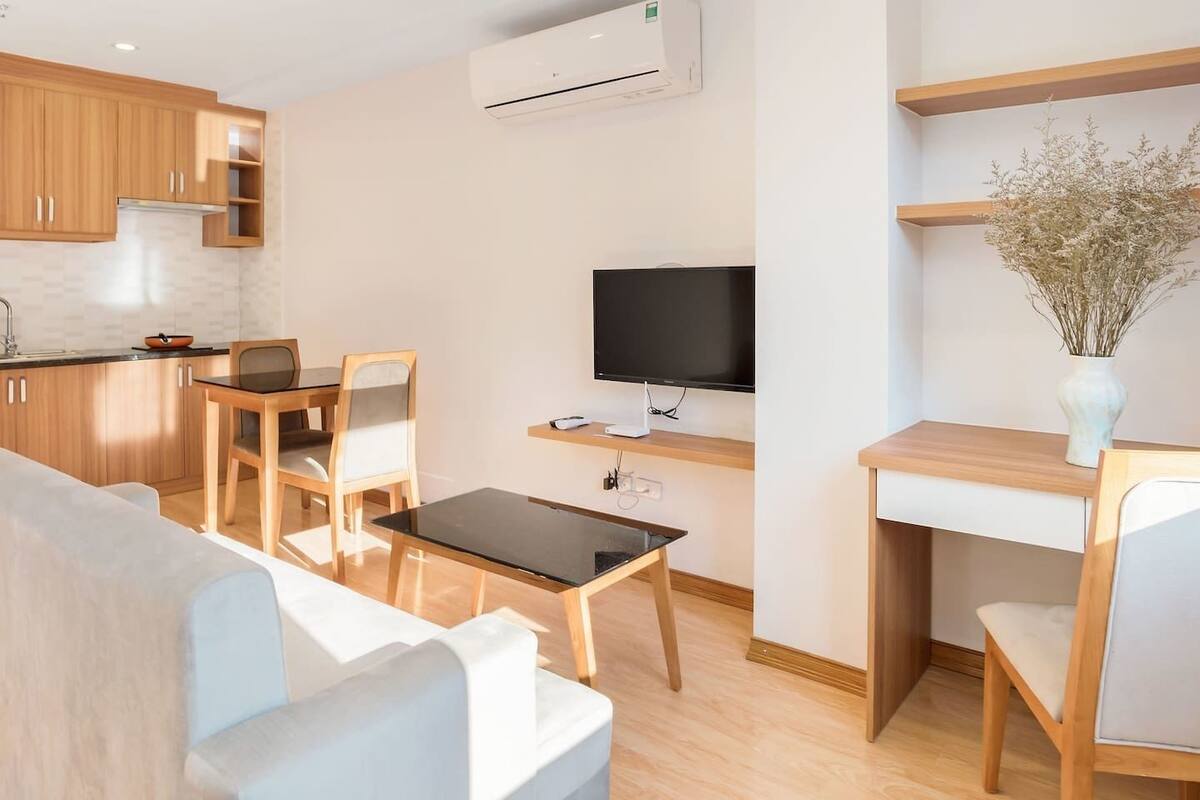 Una sala de estar moderna con un sofá, una mesa de comedor con sillas, un televisor y un pequeño escritorio con un florero.