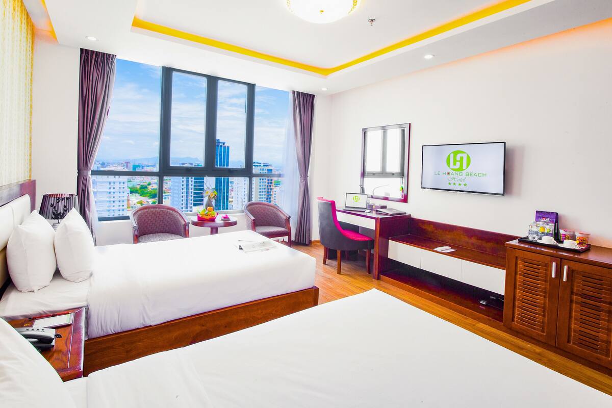 Een hotelkamer met een groot bed, een bureau met een laptop, een televisie en uitzicht op de stad.