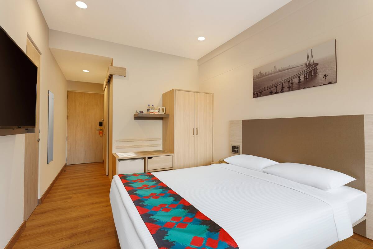 A hotel room with a bed, a desk, a wardrobe, and a painting on the wall.