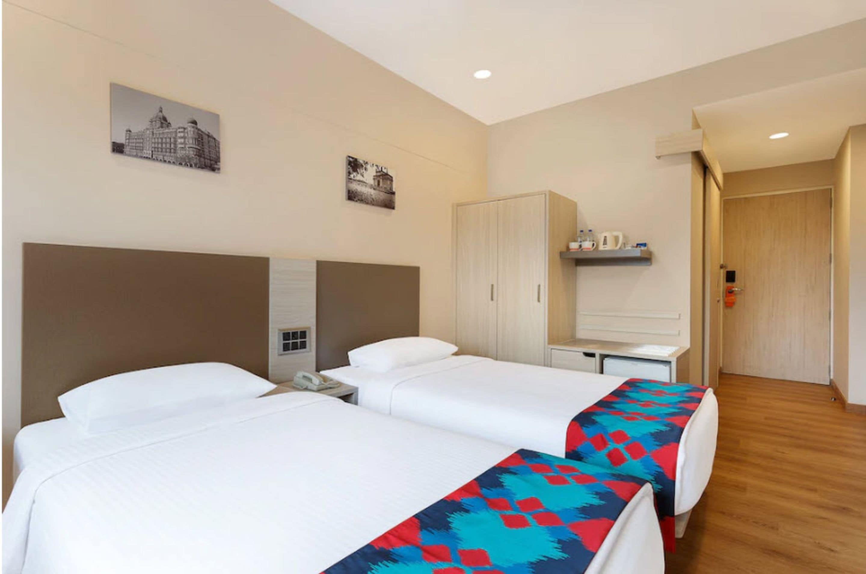 A hotel room with two beds, a wardrobe, a desk with a phone, and a shelf with toiletries.