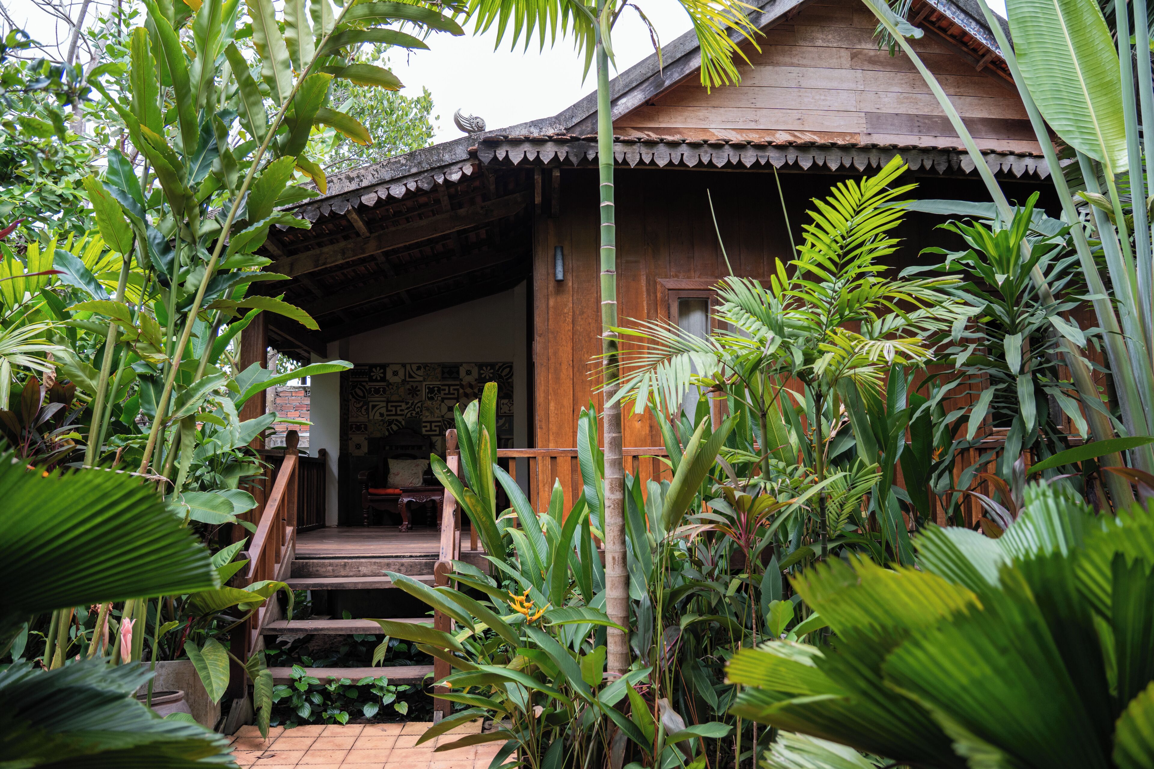 Una casa de madera con un porche rodeado de plantas tropicales.
