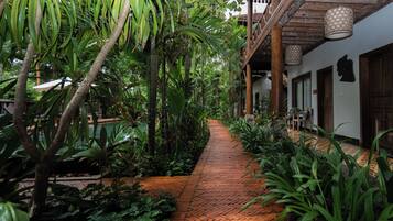 Un chemin pavé de briques, bordé d’une végétation luxuriante et de constructions en bois.