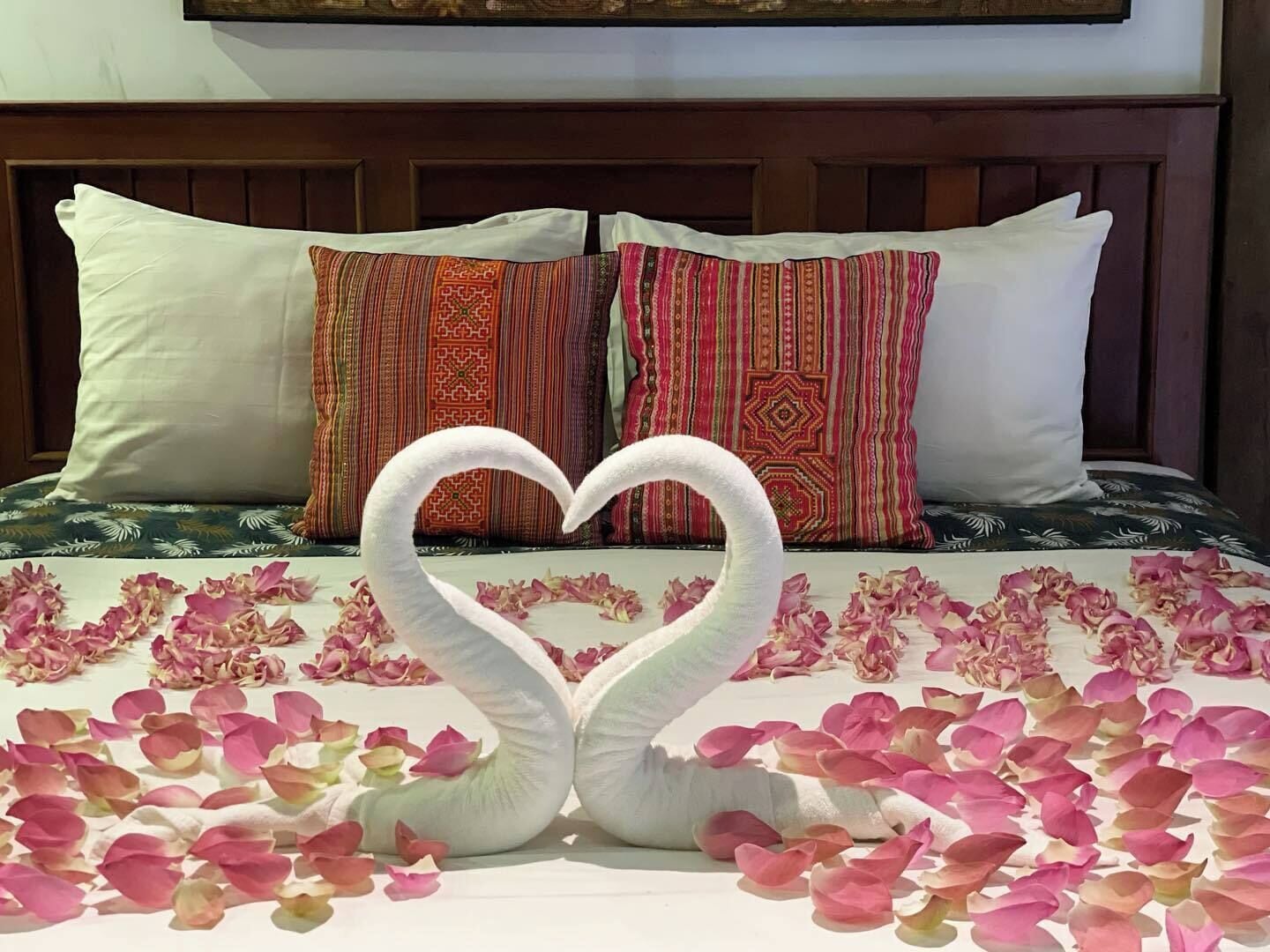 Una cama con un arreglo en forma de corazón de cisnes blancos hechos de pétalos de rosa, rodeados de más pétalos.