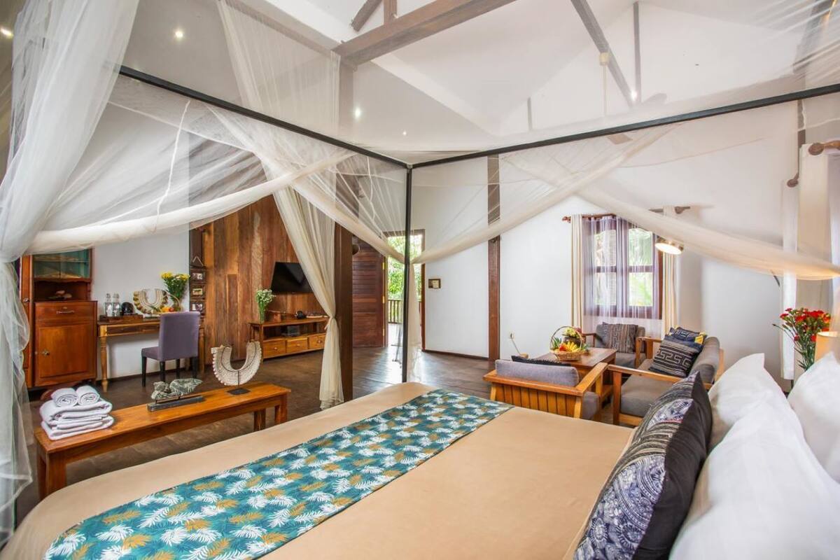 A spacious bedroom with a large bed, a desk, and a seating area with a view of the outdoors.