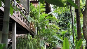 Un sendero en un jardín exuberante, con abundante follaje tropical y una estructura de madera con techo de paja.