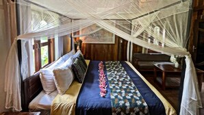 Una habitación con una cama, una mesa y una silla. La habitación tiene vigas de madera en el techo y una ventana con cortinas.