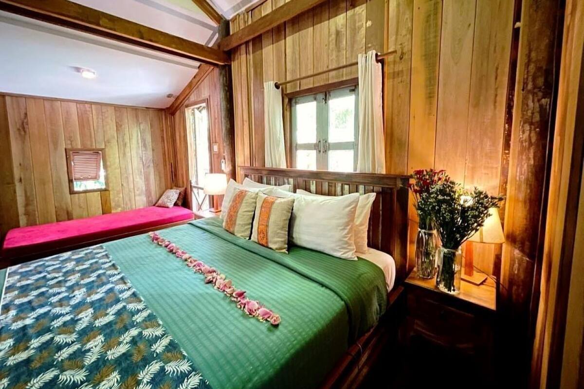 A wooden-paneled bedroom with a bed, a nightstand, and a window with curtains.