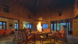 A spacious room with a large fireplace, wooden furniture, and large windows. - Tiger Mountain Pokhara Lodge (Pokhara)
