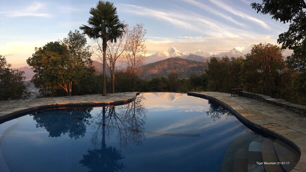A clear pool reflecting trees and mountains, surrounded by stone steps and a bench. - Tiger Mountain Pokhara Lodge (Pokhara)