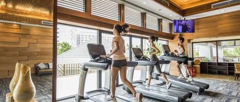 A gym with treadmills, large windows, and a TV screen.