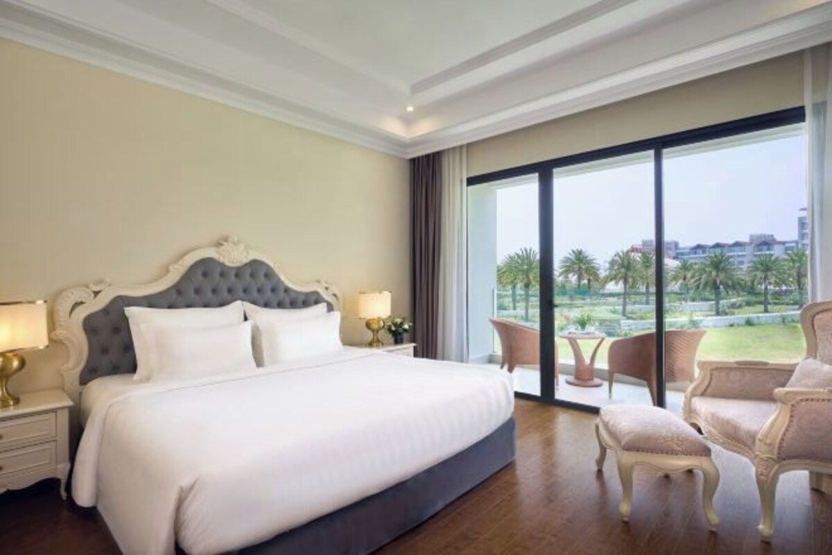 Une chambre d’hôtel avec un grand lit, une vue sur les palmiers et un balcon équipé de chaises.