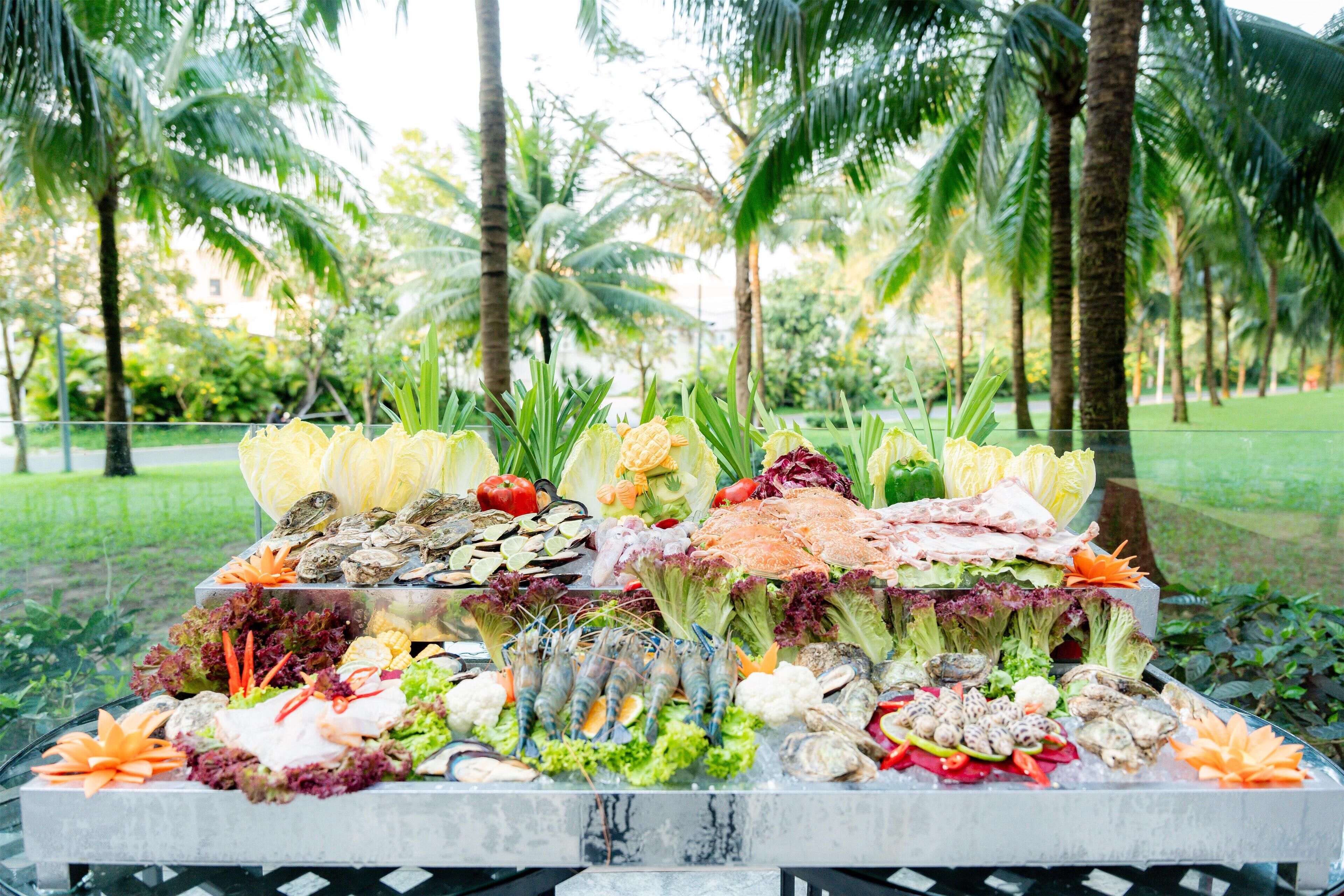 A buffet with various food items arranged on a table, set outdoors with palm trees in the background.