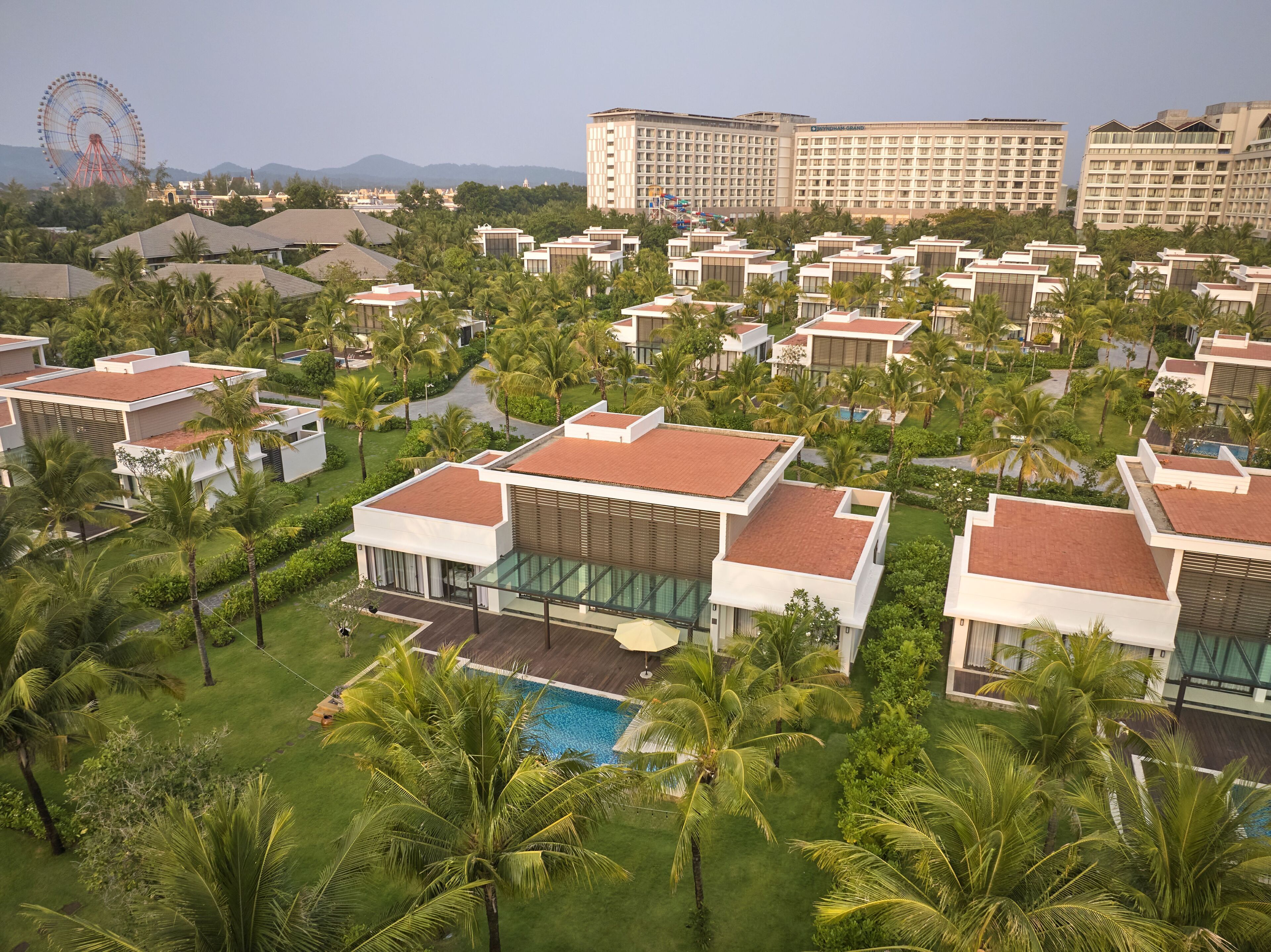 Un resort con villas modernas, una piscina y un edificio grande al fondo.