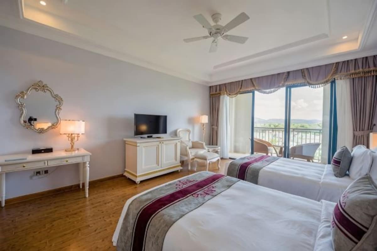 Une chambre d’hôtel avec deux lits, une télévision, un bureau avec une lampe et un balcon avec vue.