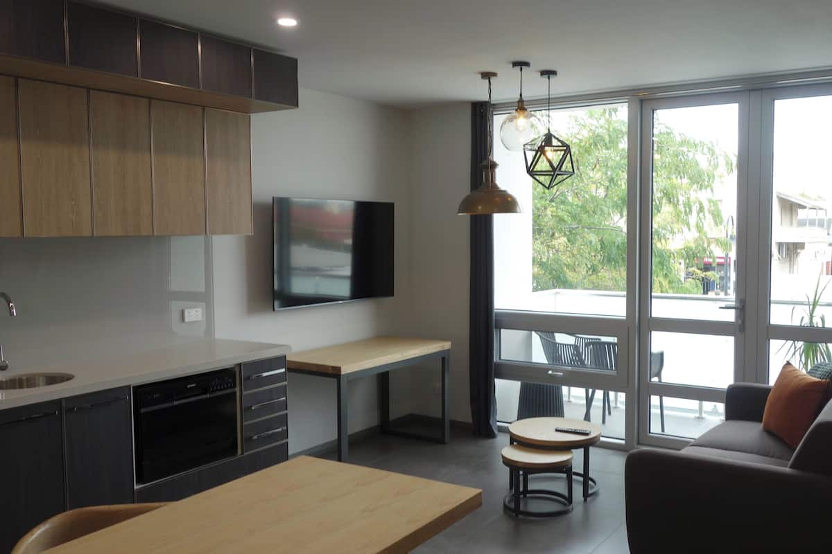 A modern kitchen with a built-in oven, a dining table, and a TV mounted on the wall.