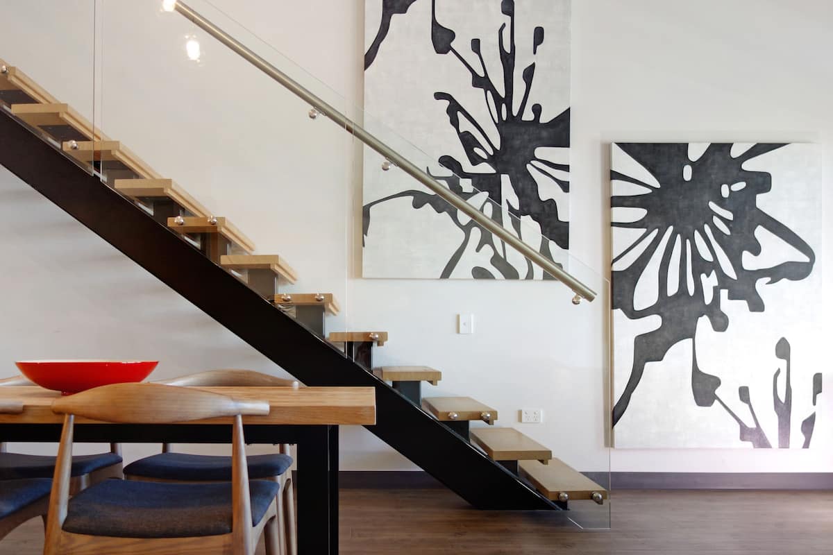 A modern interior with a wooden staircase, a dining table with chairs, and abstract wall art.