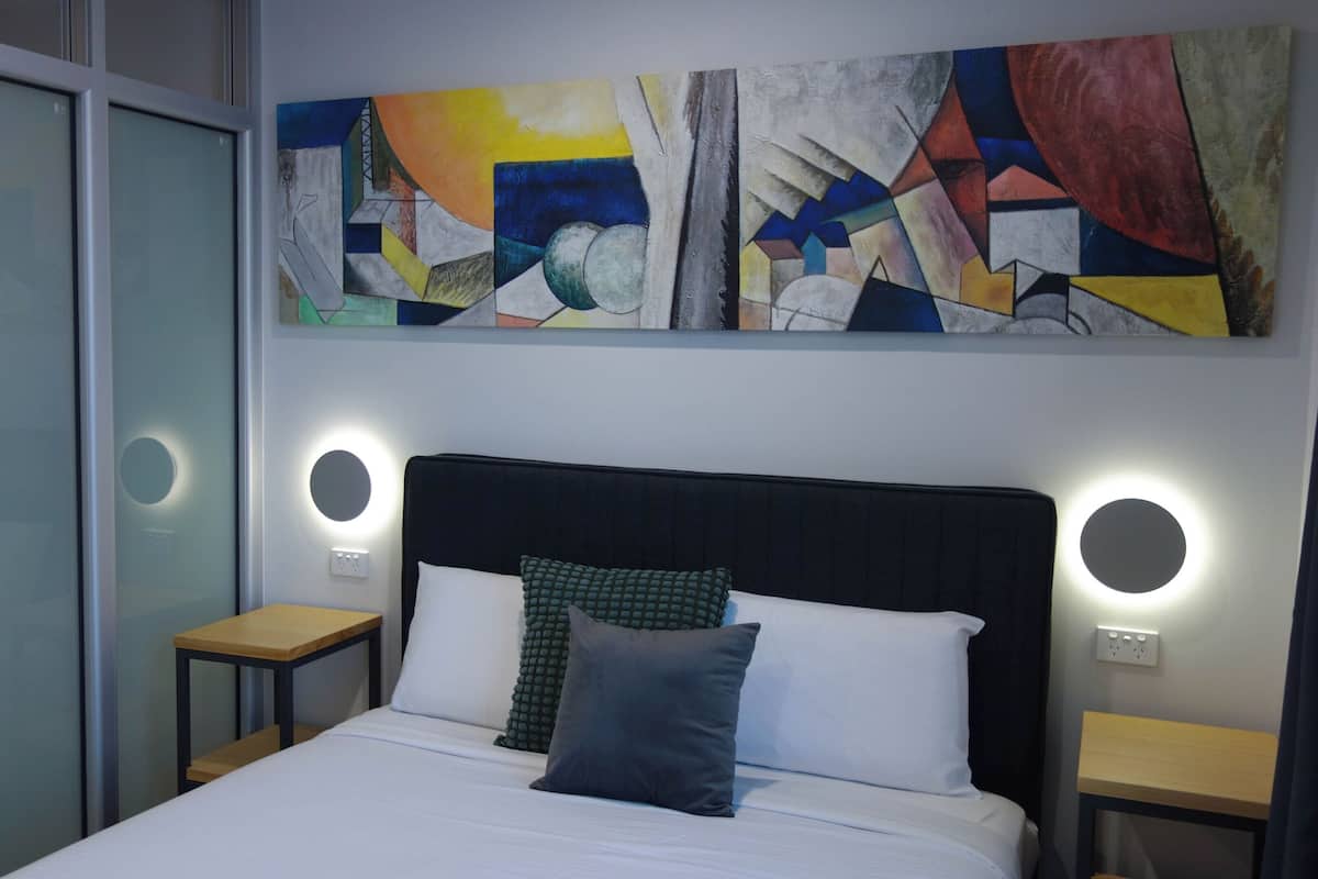 A modern hotel room with a large bed, two bedside tables, and abstract art on the wall.