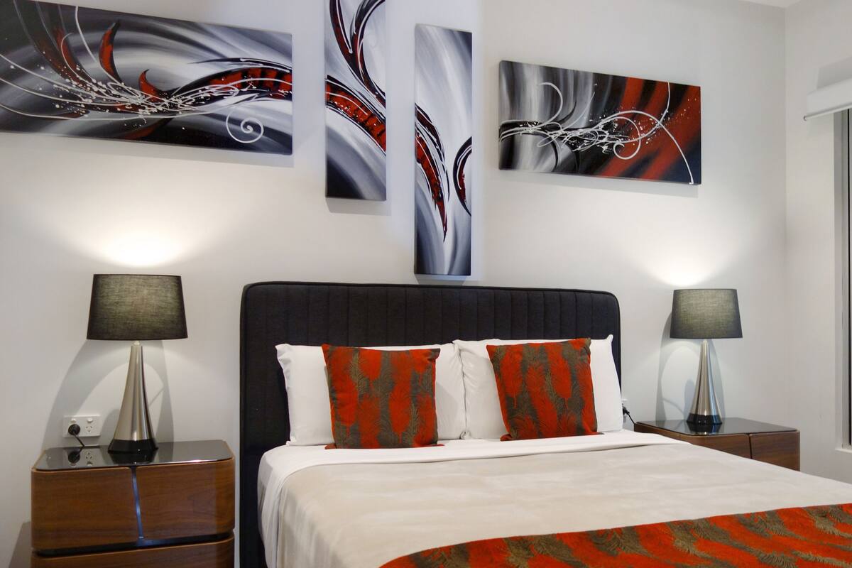 A modern bedroom with a large bed, two bedside tables, and abstract wall art.