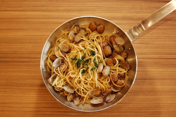 A pan of spaghetti with clams and parsley on a wooden table. - Musashino Grand Hotel And Spa (Ageo)