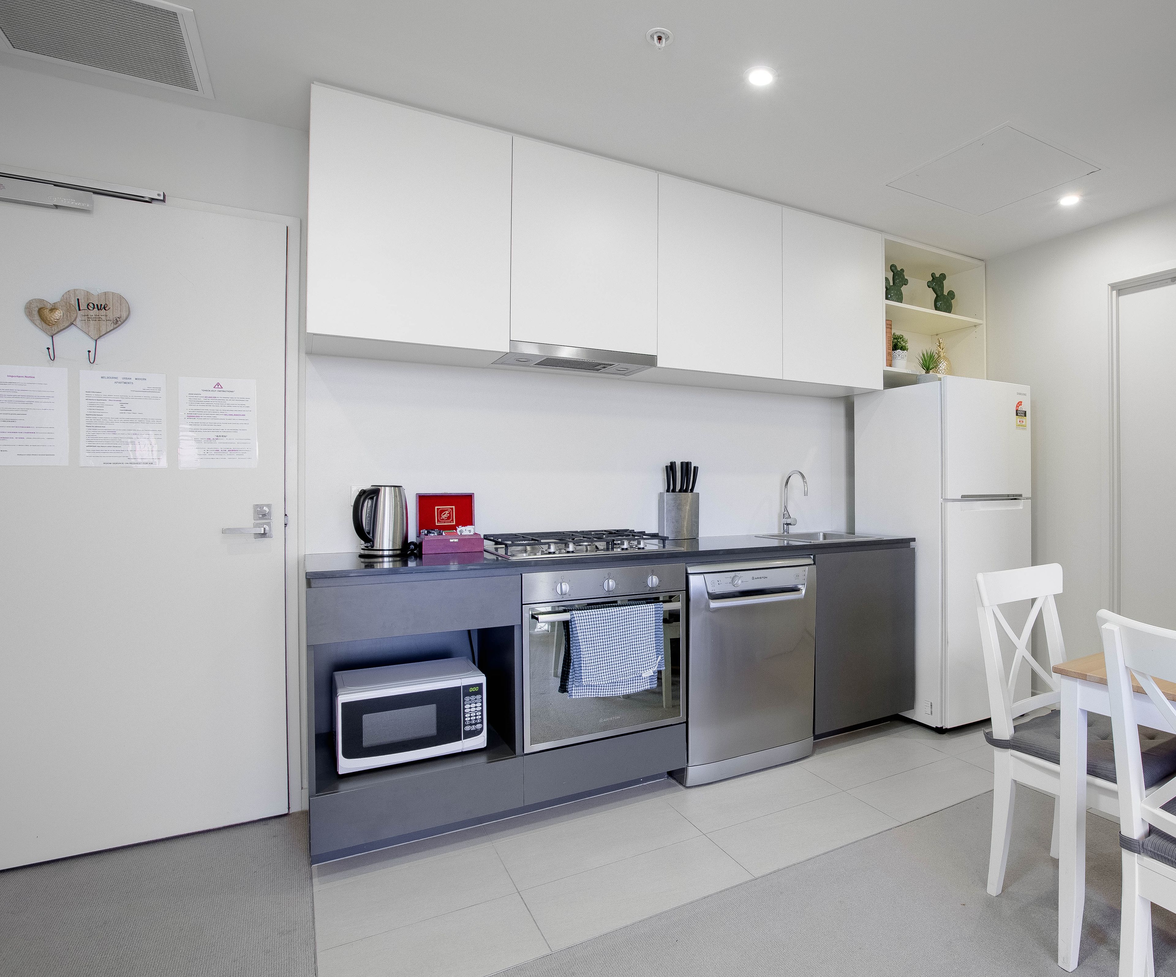 Una cocina moderna con electrodomésticos de acero inoxidable, armarios blancos y un pequeño comedor con una silla blanca.