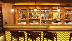 A bar area with wooden chairs, shelves of bottles, and glasses. - Hotel Grapevine (Chandauli)