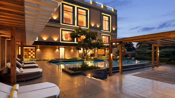 A modern building with a pool, lounge chairs, and a covered patio area. - Hotel Grapevine (Chandauli)
