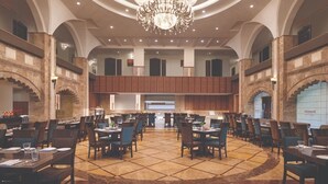 A spacious dining area with multiple tables and chairs, a central chandelier, and a modern kitchen in the background. - Hotel Grapevine (Chandauli)