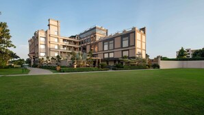 A modern multi-story building with a flat roof, surrounded by a well-maintained lawn and a few trees. - Hotel Grapevine (Chandauli)