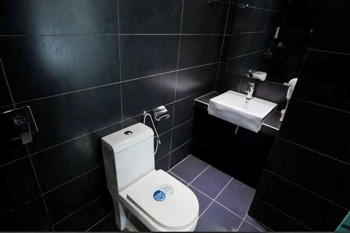 Une petite salle de bain avec des toilettes, un lavabo et des murs recouverts de carreaux sombres.