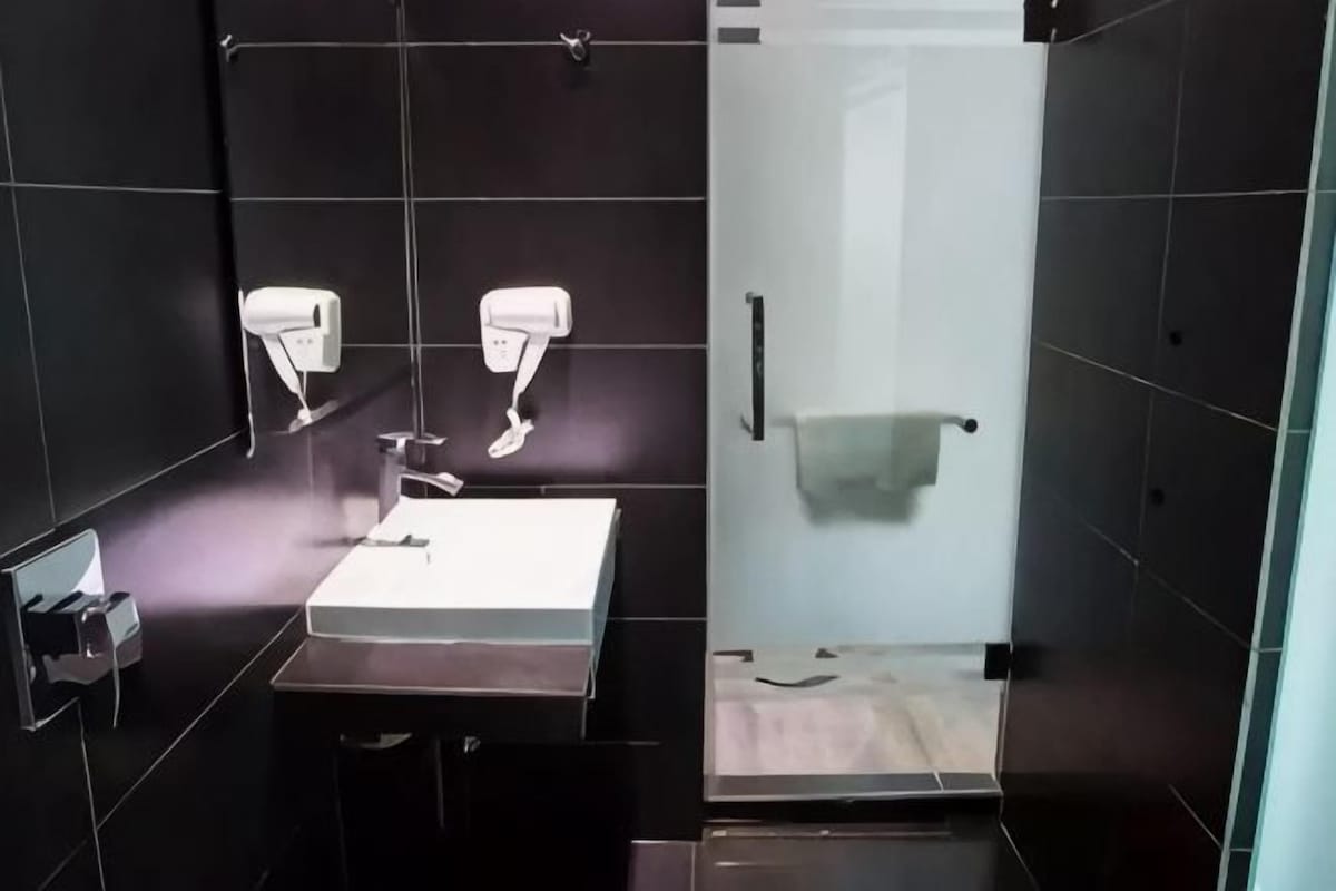 Une salle de bain avec un lavabo blanc, deux sèche-cheveux fixés au mur et une serviette suspendue à un porte-serviettes.