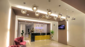 A hotel reception area with a modern design, including a reception desk, seating area, and a television screen.