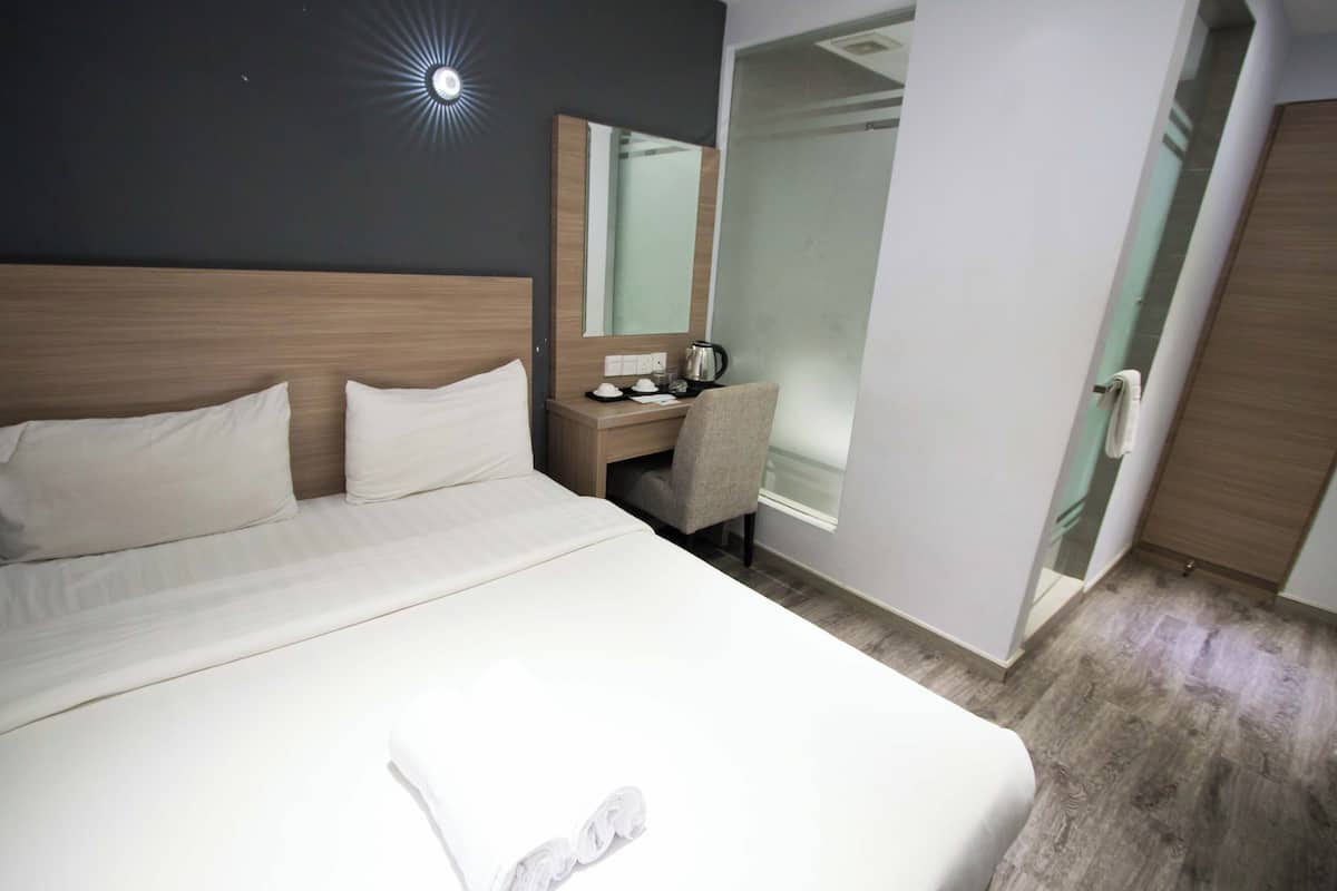 Une chambre d’hôtel avec un grand lit, une table de chevet avec une bouilloire, une chaise et un miroir.