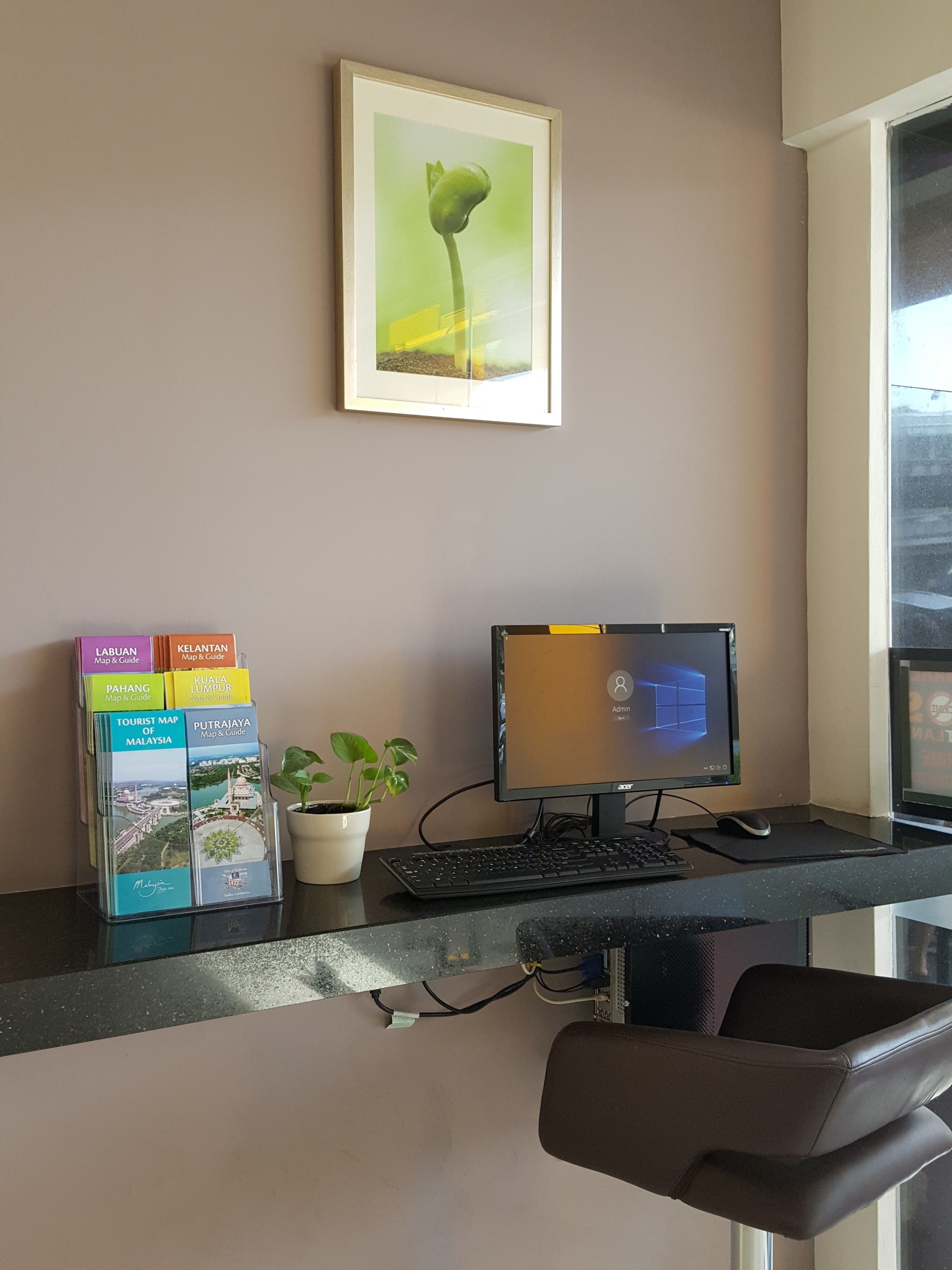 A reception desk with a computer, a potted plant, and a map stand.