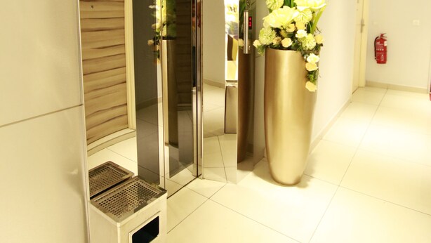 A modern hotel lobby with a reception desk, a large potted plant, and a fire extinguisher on the wall.