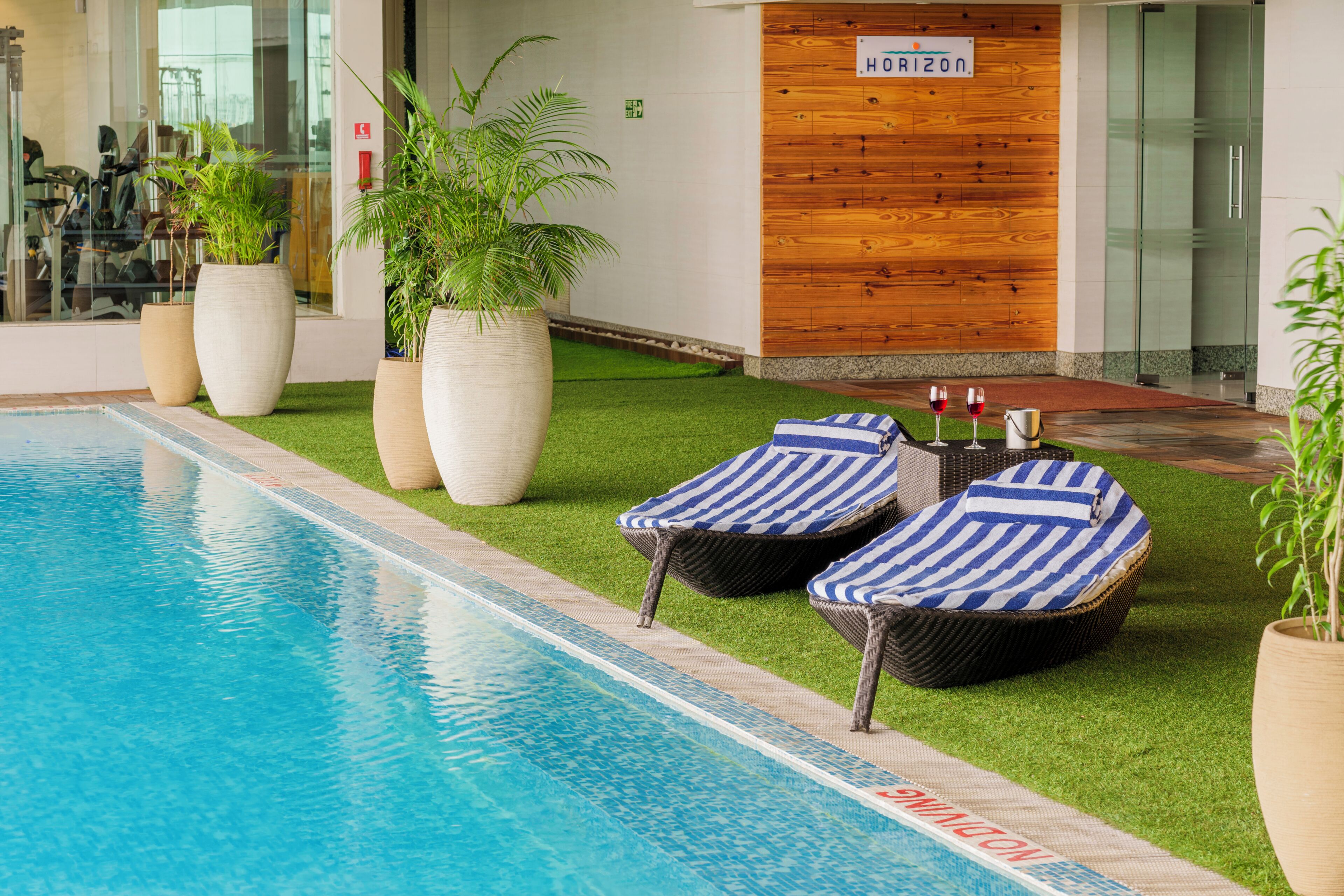 Una piscina con sillas de descanso, plantas en macetas y un muro de madera con un letrero.