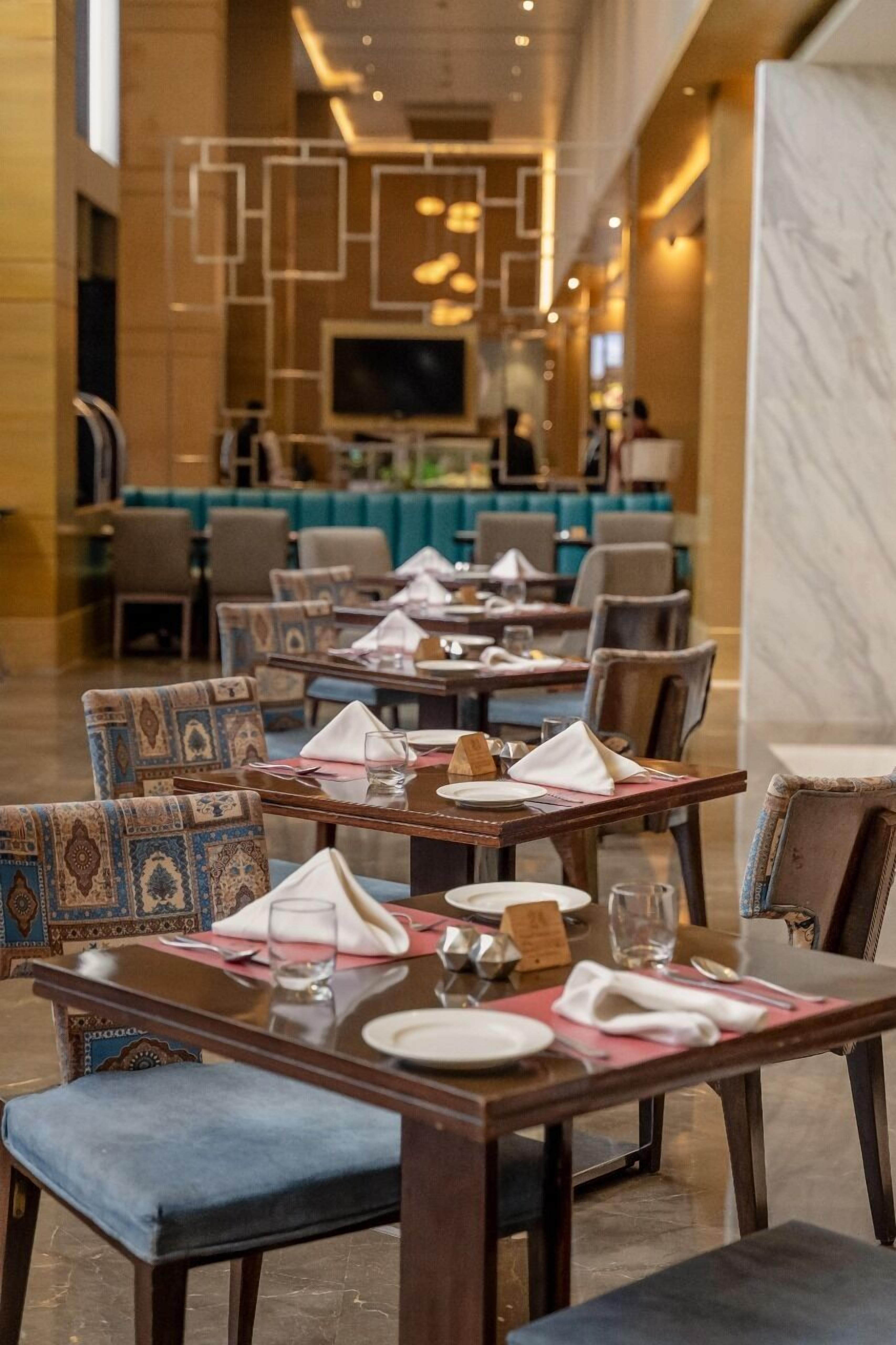 A restaurant with tables set for dining, chairs with patterned upholstery, and a bar area in the background.