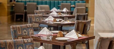 A restaurant with tables set for dining, chairs with patterned upholstery, and a bar area in the background.