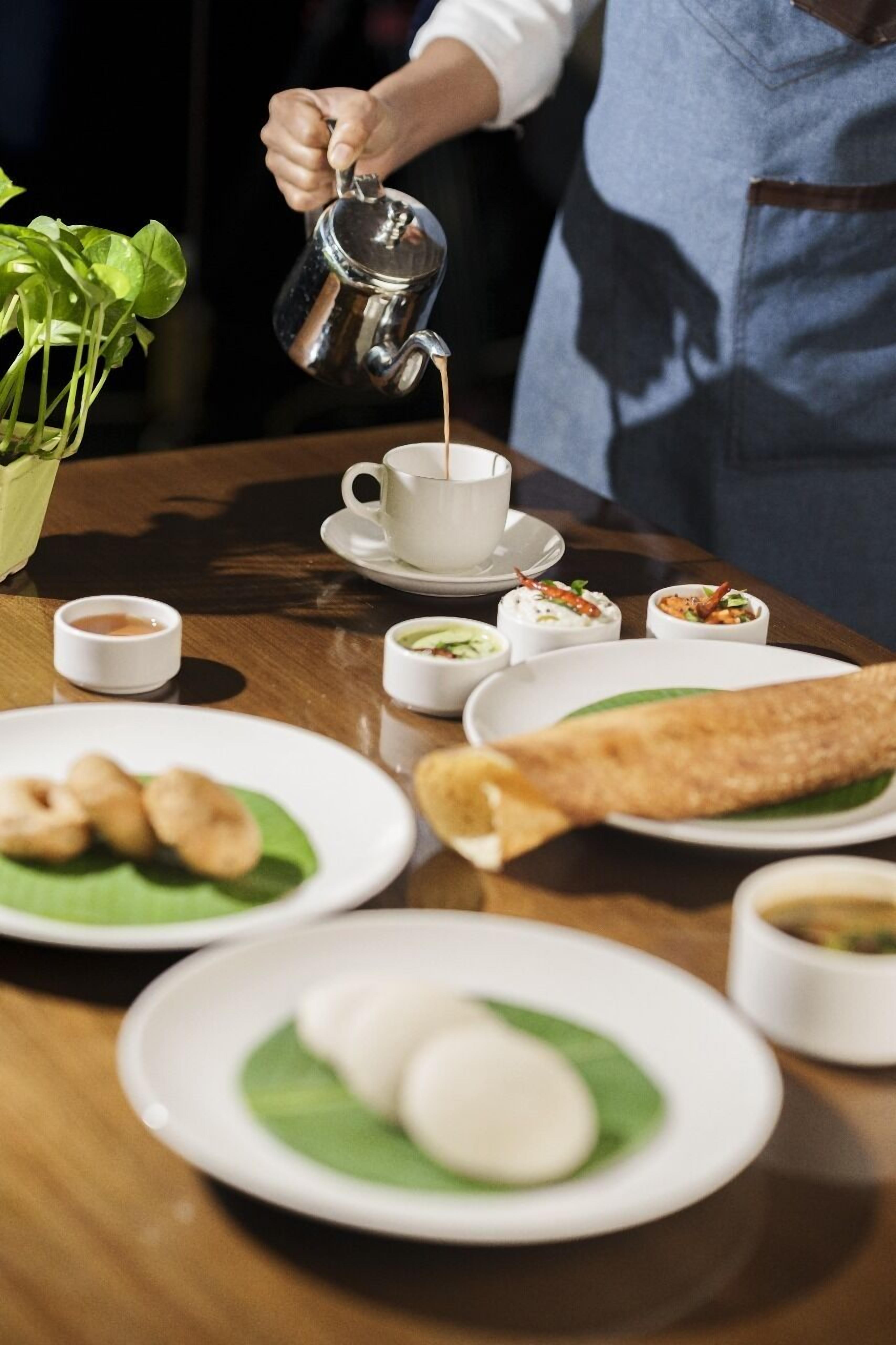 A table with various dishes, including a rolled flatbread, a cup of coffee, and several small bowls of food.