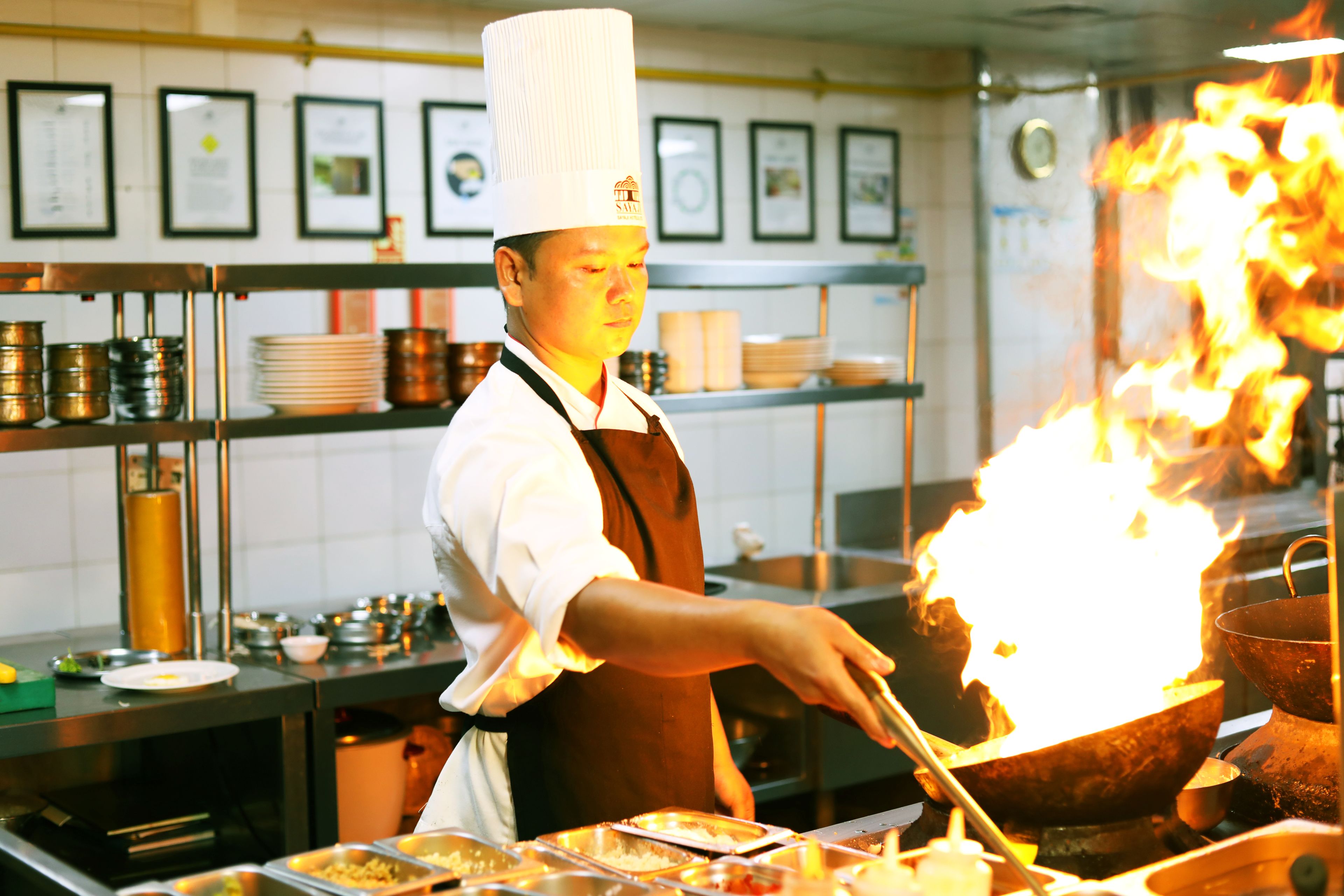 Un chef en una cocina profesional con equipo de acero inoxidable y estantes al fondo.