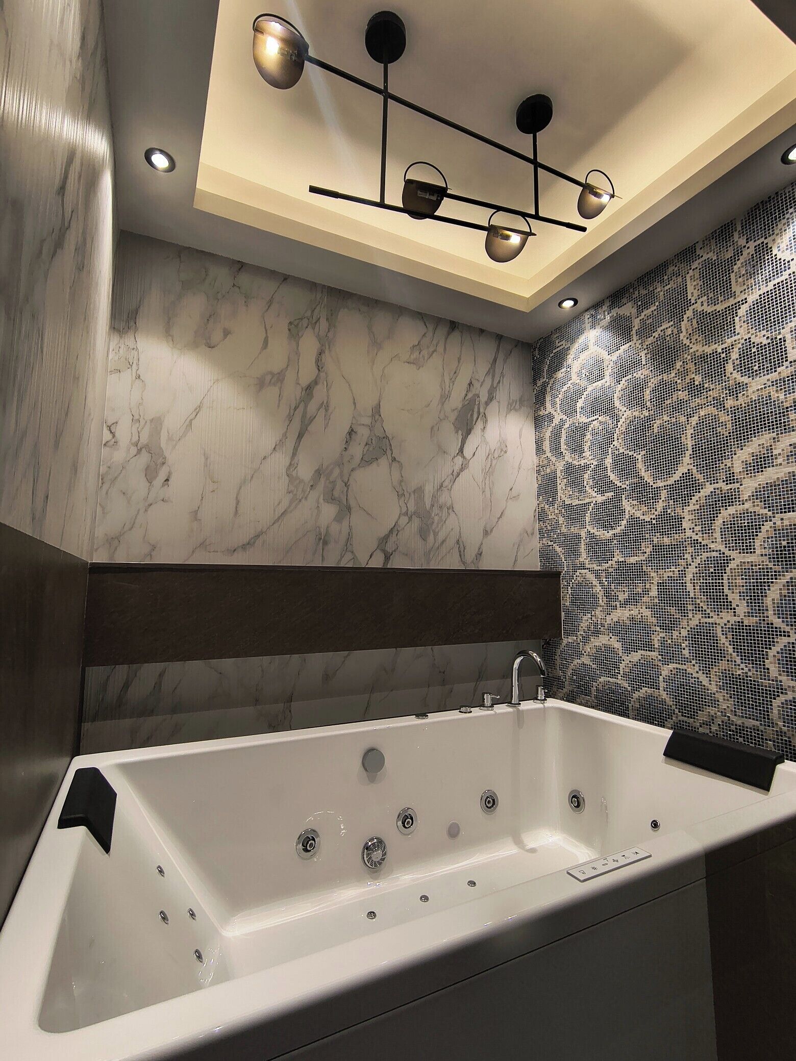 Un baño moderno con una bañera grande, una lámpara en el techo y un papel tapiz estampado.