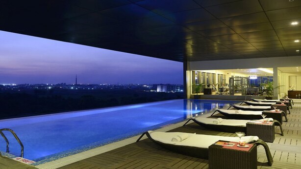 An infinity pool with lounge chairs and a view of the city at dusk. - Sayaji Raipur (Raipur)